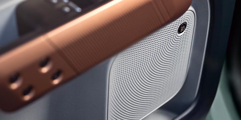 Close-up of a car's interior, showing a silver Bang & Olufsen speaker grill next to a copper-colored door handle.